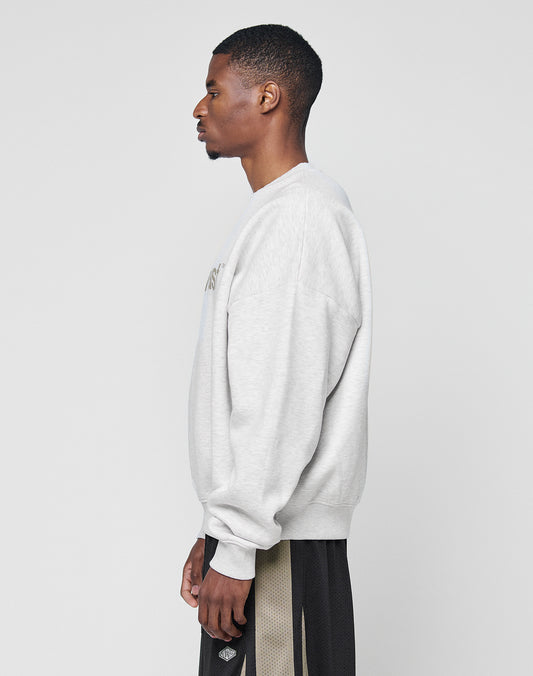A man stands in profile against a plain background, wearing the LIVE FAST DIE YOUNG Basic LiveFast Sweater in light gray and black mesh athletic shorts with beige side panels.