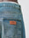 A close-up of the back pocket of Regular Denim jeans by LIVE FAST DIE YOUNG, with a brown leather LFDY patch above. The tapered leg blue jeans, worn by a person, show a visible white waistband.