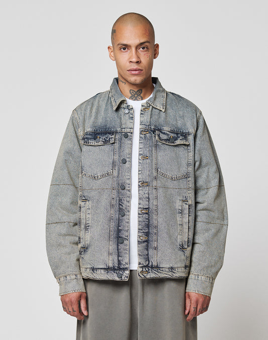 A shaved-headed person with a neck tattoo wears the LIVE FAST DIE YOUNG Puffed Denim Coach Jacket over a white shirt and gray pants, standing against a plain white background and facing the camera with a neutral expression.