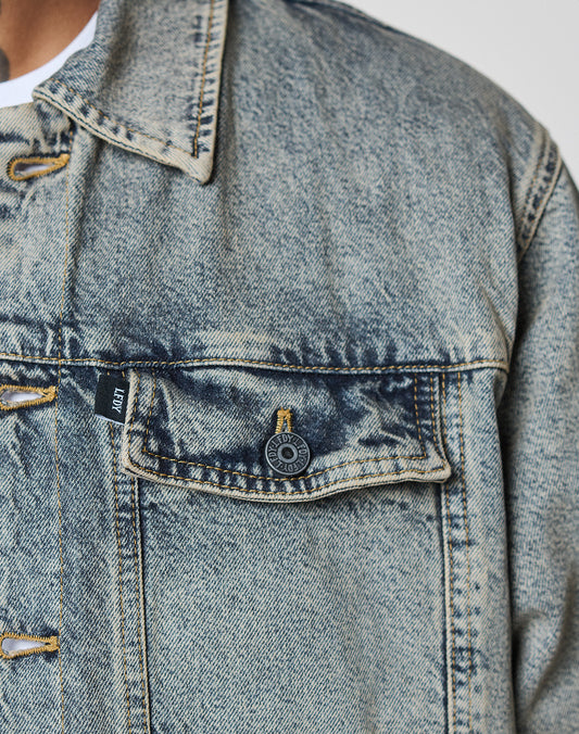 Close-up of the LIVE FAST DIE YOUNG Puffed Denim Coach Jacket in blue, highlighting the chest pocket with a black button and a small black tag by the seam; a white shirt is partially visible underneath.