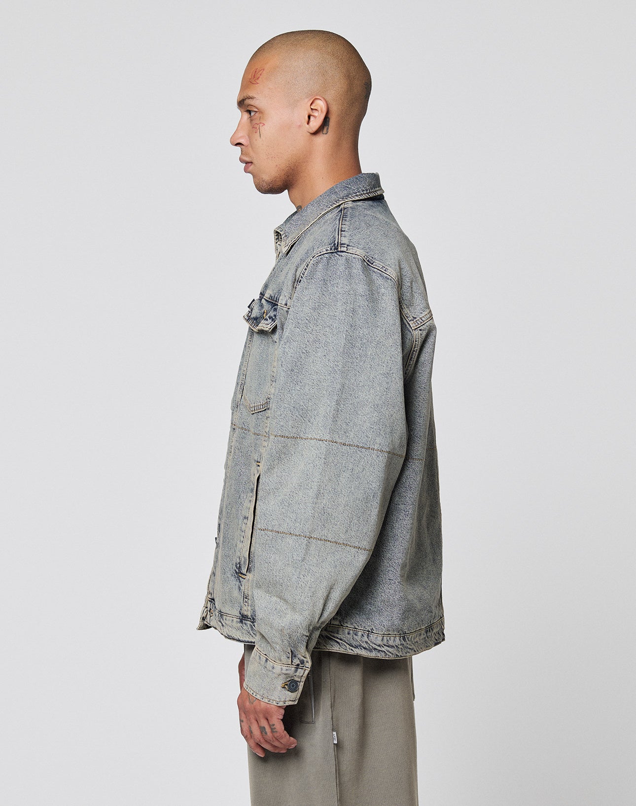 A person with a shaved head is in profile, wearing the LIVE FAST DIE YOUNG Puffed Denim Coach Jacket in light blue and light gray pants, standing against a plain light background.