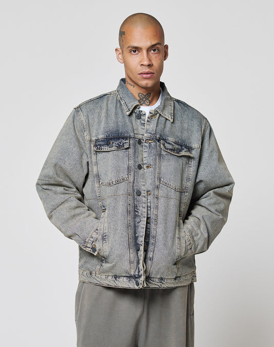 A person with a shaved head and visible neck tattoo stands facing forward, wearing a loose-fitting LIVE FAST DIE YOUNG Puffed Denim Coach Jacket and gray pants, hands in jacket pockets, against a plain background.
