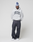 A person stands against a plain background wearing a gray LIVE FAST DIE YOUNG "Live Fast College Hooded" with an oversized fit and bold front print, styled with dark baggy jeans, white sneakers, and a white beanie featuring blue graphics. Hands in pockets, relaxed pose.