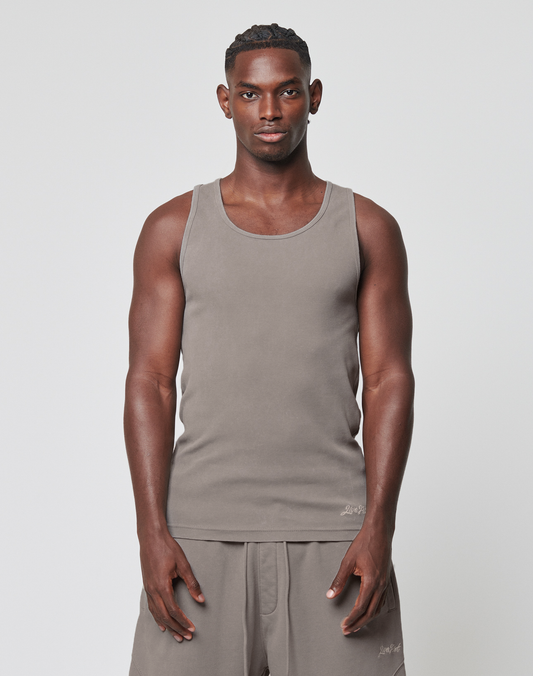 A man with short hair stands facing forward against a plain white background, wearing the LIVE FAST DIE YOUNG Basic Rib Tank in light brown and matching shorts, his arms relaxed at his sides and a neutral expression on his face. | model