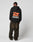 A person faces away, wearing the LFDY Hardwear Hooded by LIVE FAST DIE YOUNG—an oversized black cotton hoodie with orange and white LIVE FAST HARDWEAR graphics—paired with loose brown jeans and white shoes against a plain light background.