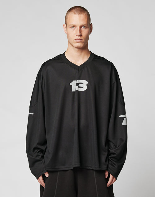 A person with short hair wears the LIVE FAST DIE YOUNG Live Fast Jersey, a loose-fitting, long-sleeve black oversize shirt with the number 13 in white on the chest and sleeve numbers, standing against a plain light background.