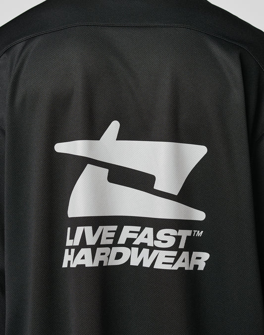 A close-up of the back of the black Live Fast Jersey by LIVE FAST DIE YOUNG, made from 100% polyester, shows a bold, reflective graphic logo above the words LIVE FAST HARDWEAR in uppercase letters.