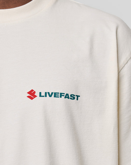 Close-up of the LFDY Dealership Tee by LIVE FAST DIE YOUNG, an oversized cream T-shirt made from 100% cotton, with a red geometric logo and bold green "LIVEFAST" print on the left chest.