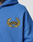 A close-up of the blue LIVE FAST DIE YOUNG LFDY Team Hooded Zip in an oversize fit, showcasing a gold embroidered laurel wreath with L.F.D.Y at the center. Part of a person's neck and shoulder is visible.