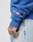 A person wears light denim jeans and the LFDY Team Hooded Zip by LIVE FAST DIE YOUNG in Oversize Fit, featuring multilogo embroidery plus UK, Netherlands, and Germany flag patches on the sleeve. Unique tattoos are visible on their hand.