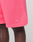 Close-up of a person wearing bright pink Basic Shorts by LIVE FAST DIE YOUNG, featuring an elastic waistband and white LFDY™ logo print near the hem, set against a plain neutral background.