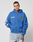 A man in the LIVE FAST DIE YOUNG LFDY Team Hooded Zip with Multilogo Stickereien and light blue jeans stands against a plain white background, looking directly at the camera with a neutral expression.