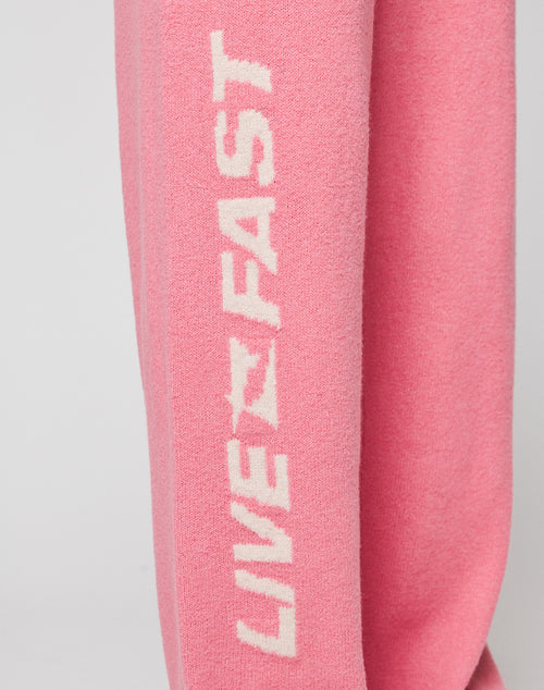 Close-up of pink fabric on the Live Fast Boucle Pants by LIVE FAST DIE YOUNG, with bold white "LIVE FAST" lettering printed vertically along the leg, featuring a straight leg (gerades Bein) and elastic waistband.