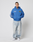 A person stands against a plain white background wearing the blue LFDY Team Hooded Zip by LIVE FAST DIE YOUNG with Multilogo Stickereien, light blue oversized baggy jeans, and white sneakers, hands in pockets and a neutral expression.