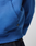 Close-up of a person wearing the blue LFDY Team Hooded Zip by LIVE FAST DIE YOUNG, featuring a small black AGI tag near the pocket and Multilogo Stickereien accents, paired with dark denim jeans. The background is plain and out of focus.