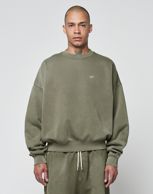 A person wears the LIVE FAST DIE YOUNG Basic Chest Sweater in olive green with a handmade fade effect and matching sweatpants, standing facing forward against a light gray background. The oversize fit sweater features small chest text.