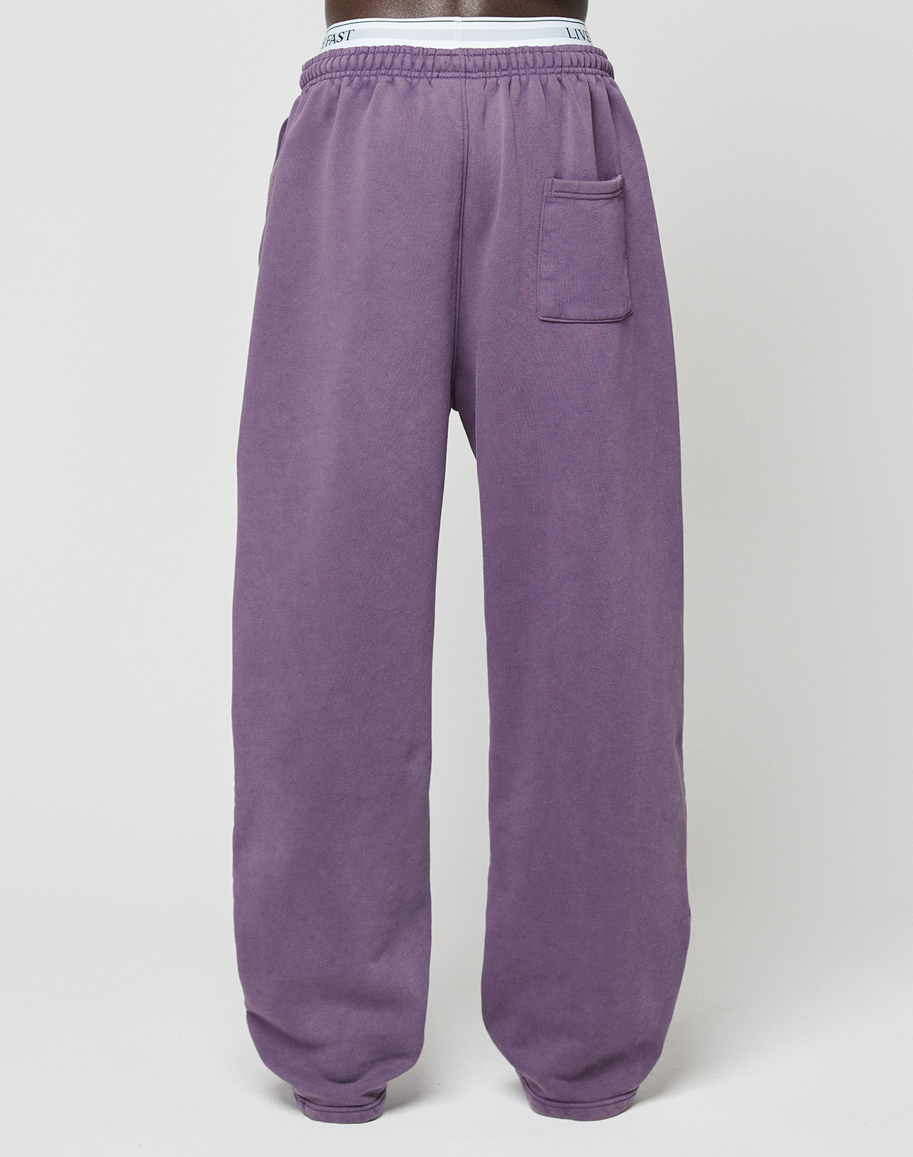 The LIVE FAST DIE YOUNG Basic Wide Jogger sweatpants feature a purple color, elastic waistband, single right patch pocket, and relaxed wide-leg fit. Displayed on a plain white background.