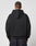A person with short hair stands with their back to the camera, wearing the LIVE FAST DIE YOUNG LFDY Team Hooded Zip in black with Multilogo Stickereien and dark jeans, set against a plain light grey background.