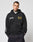 A man stands facing forward with hands in pockets, wearing the black LFDY Team Hooded Zip by LIVE FAST DIE YOUNG featuring white and gold Multilogo Stickereien, against a plain light background.
