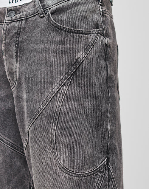 Close-up of Tribal Wide Denim jeans by LIVE FAST DIE YOUNG, featuring gray fabric, unique curved stitching, tribal panels, a white waistband detail, metal button top, and a baggy fit for comfort and style.