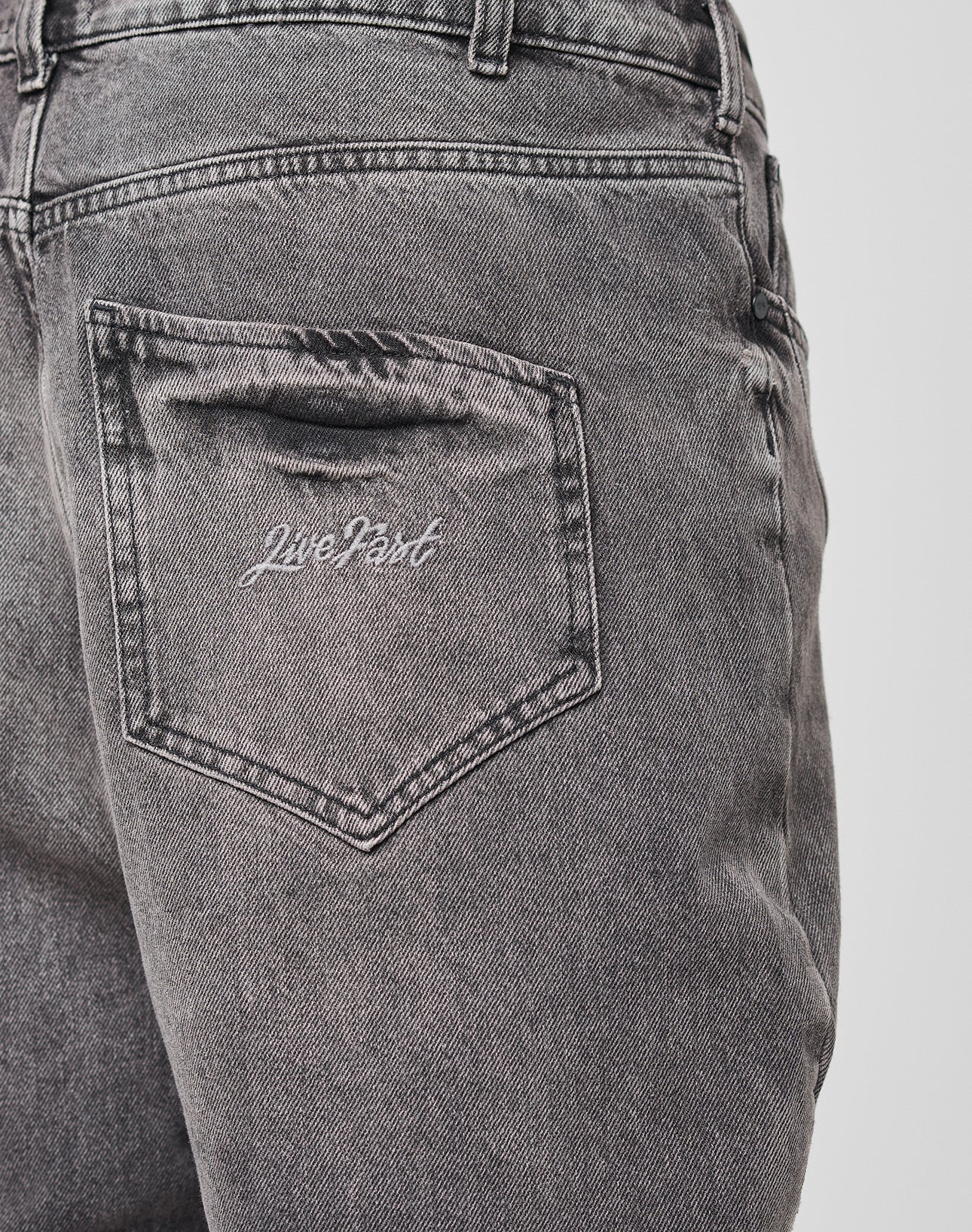 Close-up of the back pocket of Tribal Wide Denim jeans by LIVE FAST DIE YOUNG, featuring Tribal Panels and "Live Fast" embroidered in white on 100% Baumwolle fabric.