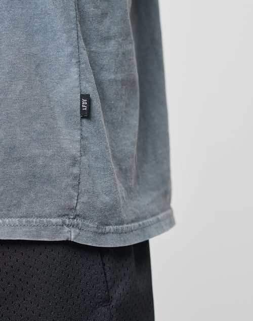 Close-up of the lower side of a gray Basic Muscle Shirt by LIVE FAST DIE YOUNG with a small black ROV tag, paired with black textured shorts. The background is plain and light-colored.