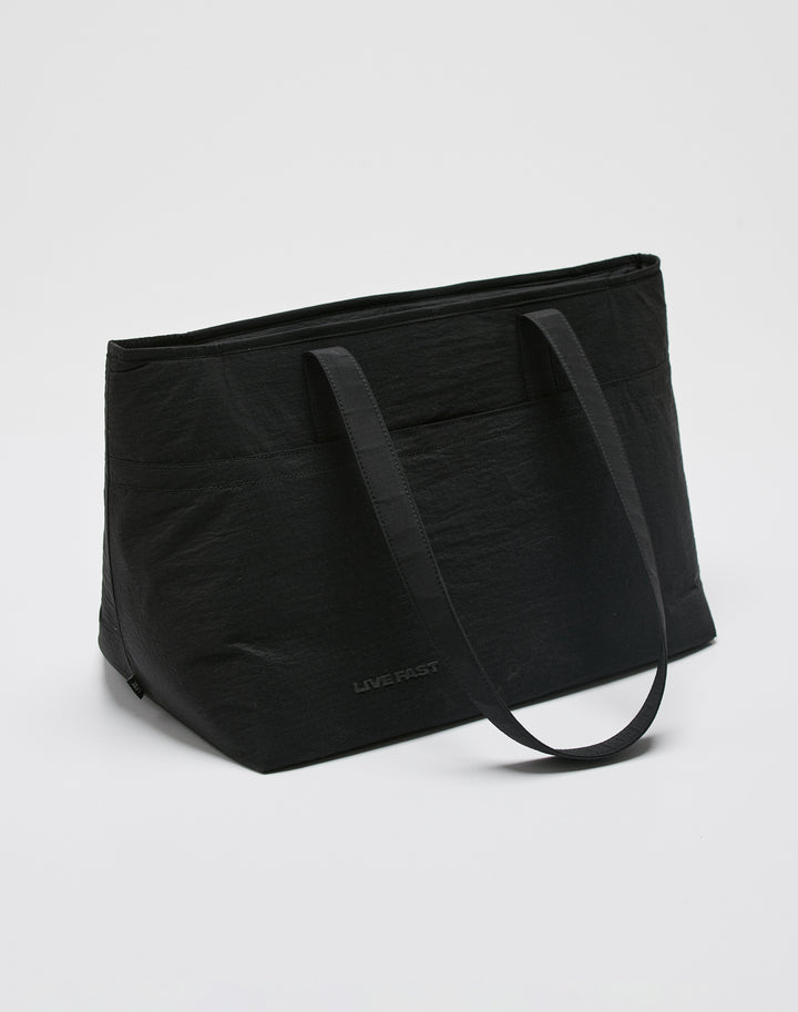 The LIVE FAST DIE YOUNG Live Fast Paintbag is a large black nylon tote with two shoulder straps, subtle LIVE FAST branding near the bottom, and a secure zip closure, shown against a plain white background.