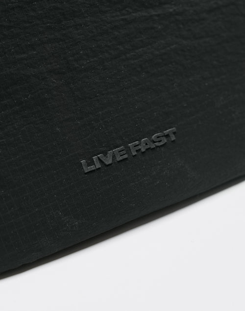 Close-up of the textured black surface of the LIVE FAST DIE YOUNG Live Fast Paintbag, featuring LIVE FAST embossed in capitals near the center. The lower part transitions into a smooth white background.