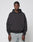 A man with braided hair wears a loose-fitting black LFDY Monaco Boys Hooded by LIVE FAST DIE YOUNG and light blue jeans, standing against a plain light gray background. The hoodie is crafted from Baumwolle Polyester for comfort.
