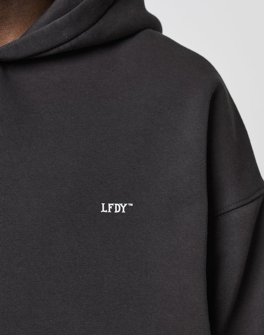 Close-up of the LIVE FAST DIE YOUNG LFDY Monaco Boys Hooded in black, featuring white LFDY™ chest print. Only shoulder, hood, and chest are shown. Oversize fit and premium cotton-poly mix offer optimal comfort.