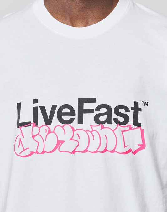 A person wearing the LIVE FAST DIE YOUNG Basic Live Fast Graffiti Tee, a regular fit white 100% Baumwolle T-shirt featuring a bold black "LiveFast" frontprint above pink graffiti-style writing.
