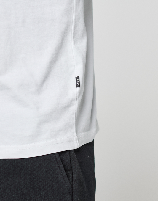 Close-up of a person wearing the LIVE FAST DIE YOUNG Basic Live Fast Graffiti Tee (100% Baumwolle, white, small black side tag) with black pants, standing against a plain light gray background.
