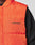Close-up of a person wearing the LIVE FAST DIE YOUNG "Live Fast Cropped Vest" in bright orange with Druckknöpfe and black "LIVE FAST" print, layered over a black textured long-sleeve shirt.