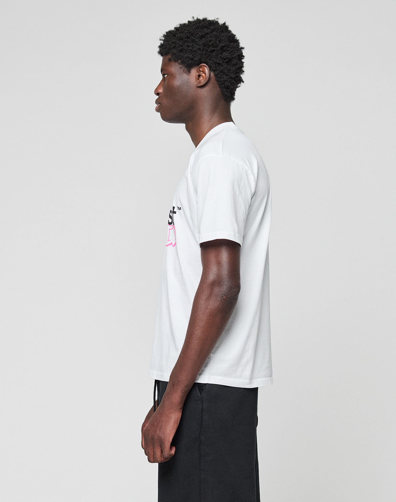 A man with short curly hair stands in profile against a plain background, wearing the LIVE FAST DIE YOUNG Basic Live Fast Graffiti Tee in white and black pants.