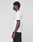 A man with short curly hair stands in profile against a plain background, wearing the LIVE FAST DIE YOUNG Basic Live Fast Graffiti Tee in white and black pants.