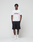 A man faces forward against a white background, wearing the LIVE FAST DIE YOUNG Basic Live Fast Graffiti Tee in regular fit (100% Baumwolle), black shorts, white socks, and white sneakers. His arms rest relaxed at his sides.