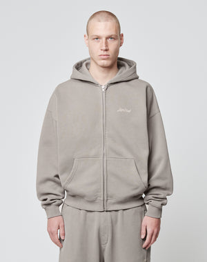 A person with a shaved head wears the LIVE FAST DIE YOUNG Basic Script Hooded Zip—a loose-fitting, gray Baumwolle-Polyester hoodie and sweatpants—standing against a light gray background, looking at the camera with a neutral expression.