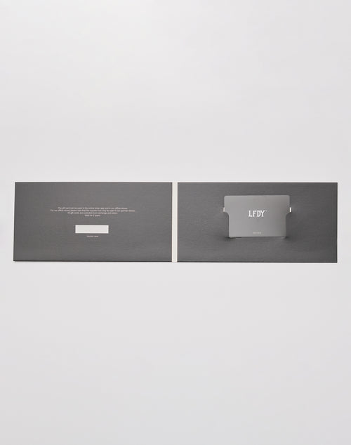 A flat, open black card holder from LIVE FAST DIE YOUNG displays the Gutschein | Gift Card with silver labeling. Text is printed left, the card fits right, all shown as an elegante Geschenkverpackung on a light gray background.