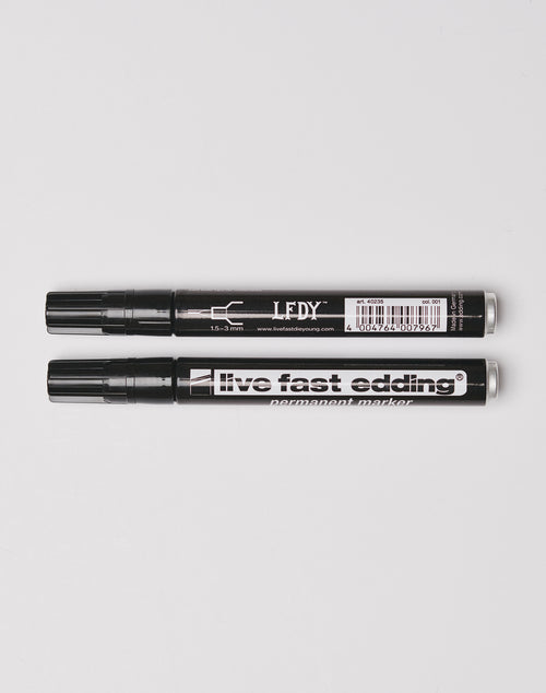 Two black permanent markers with caps rest side by side on a white surface—one labeled LEDY, the other Live Fast Edding by LIVE FAST DIE YOUNG; both are wasserfest and perfect for making lasting marks.