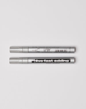 Two silver Live Fast Edding markers from LIVE FAST DIE YOUNG are laid parallel on a white surface; the top shows branding and barcode, while the bottom displays live fast edding paint marker.