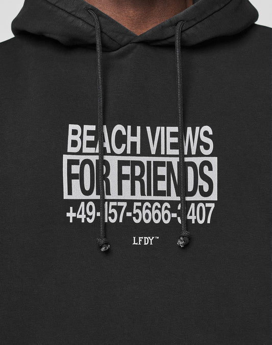 Close-up of the black Live Fast Call Us Hooded by LIVE FAST DIE YOUNG in Oversize Fit, featuring a white BEACH VIEWS FOR FRIENDS +49-157-5666-1407 LFDY™ front print and black drawstrings.