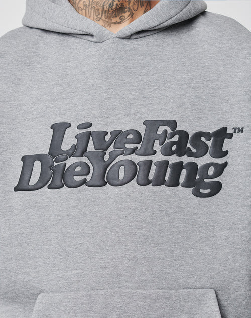 Close-up of a gray Basic Hooded by LIVE FAST DIE YOUNG with bold black text. The persons neck and a tattoo are visible above the oversized fit hoodie.