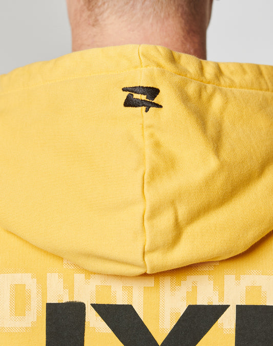 Close-up of the back of a person wearing the LIVE FAST DIE YOUNG Print Over Hooded, an oversized yellow hoodie with a small black logo at the top center and large black-and-white print on the front and back.