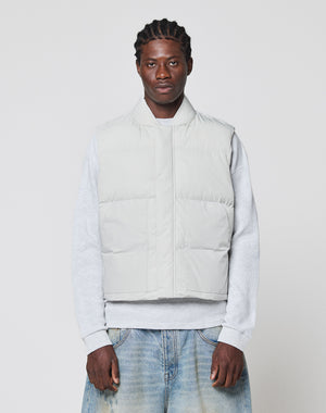 A man with short, braided hair and a neutral expression wears the LIVE FAST DIE YOUNG Basic Cropped Vest in light gray polyester over a gray sweatshirt and loose blue jeans, standing against a plain background. The vest offers a regular fit for everyday comfort.