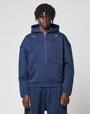 A person with short dreadlocks wears the LIVE FAST DIE YOUNG LFDY Active Fleece Hooded Zip and matching pants in navy blue, featuring curved seam details and small white logo text on the chest, against a light gray background.