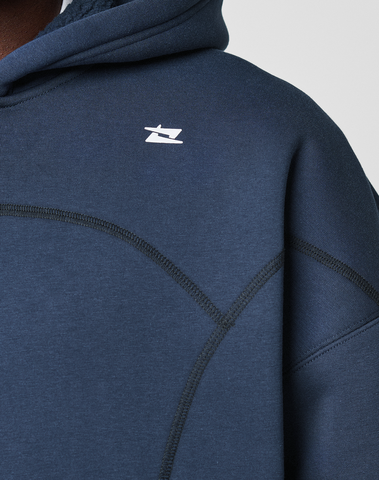 A close-up of a person wearing the LIVE FAST DIE YOUNG LFDY Active Fleece Hooded Zip in dark blue, featuring an oversize fit, black stitch details, and a small white abstract logo on the chest. The hood is up; only the upper torso is visible.
