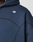 A close-up of a person wearing the LIVE FAST DIE YOUNG LFDY Active Fleece Hooded Zip in dark blue, featuring an oversize fit, black stitch details, and a small white abstract logo on the chest. The hood is up; only the upper torso is visible.