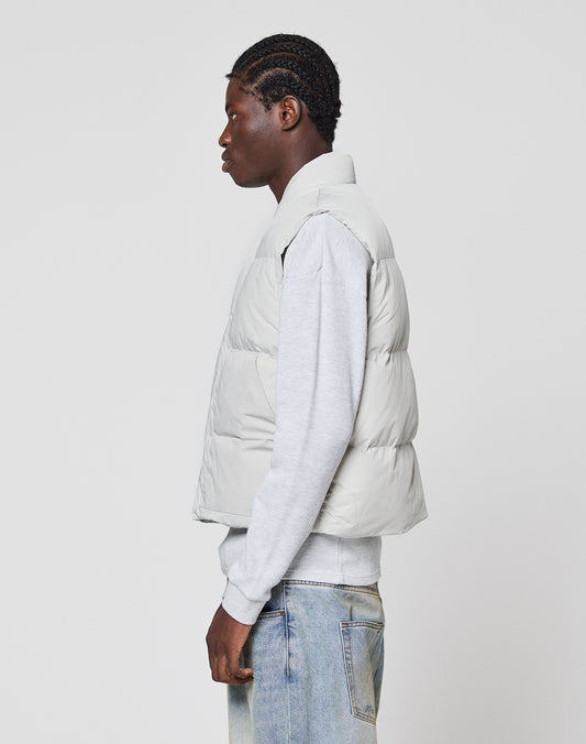 A person stands in profile against a plain white background, wearing the LIVE FAST DIE YOUNG Basic Cropped Vest in light grey polyester over a grey sweatshirt and light blue jeans.