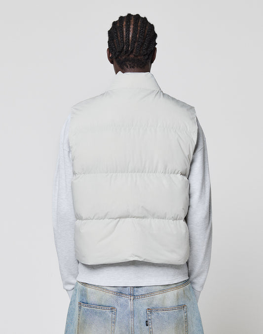 A person with braided hair, seen from behind, wears the LIVE FAST DIE YOUNG Basic Cropped Vest in light gray polyester over a gray sweatshirt and light blue jeans against a plain light background.