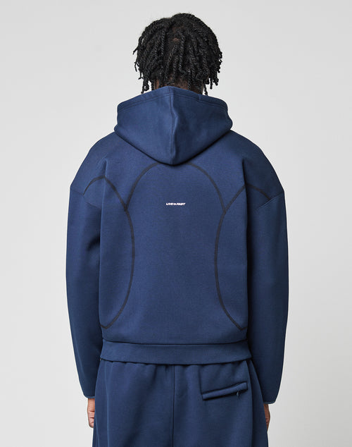 A person with short, twisted hair is seen from behind wearing the LIVE FAST DIE YOUNG LFDY Active Fleece Hooded Zip in navy blue, featuring an oversize fit, black seam details, and a small white logo print centered on the back.